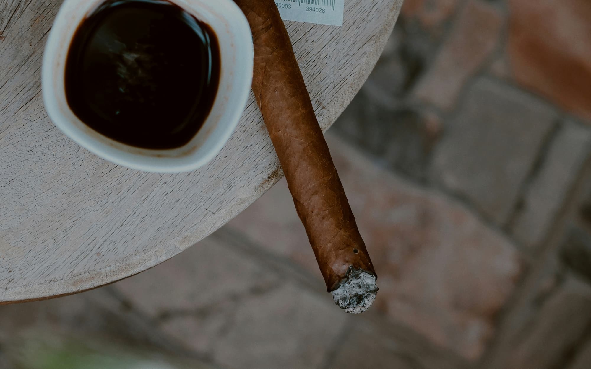 Partially smoked cigar shown sitting on a table, paired with a cup of black coffee.