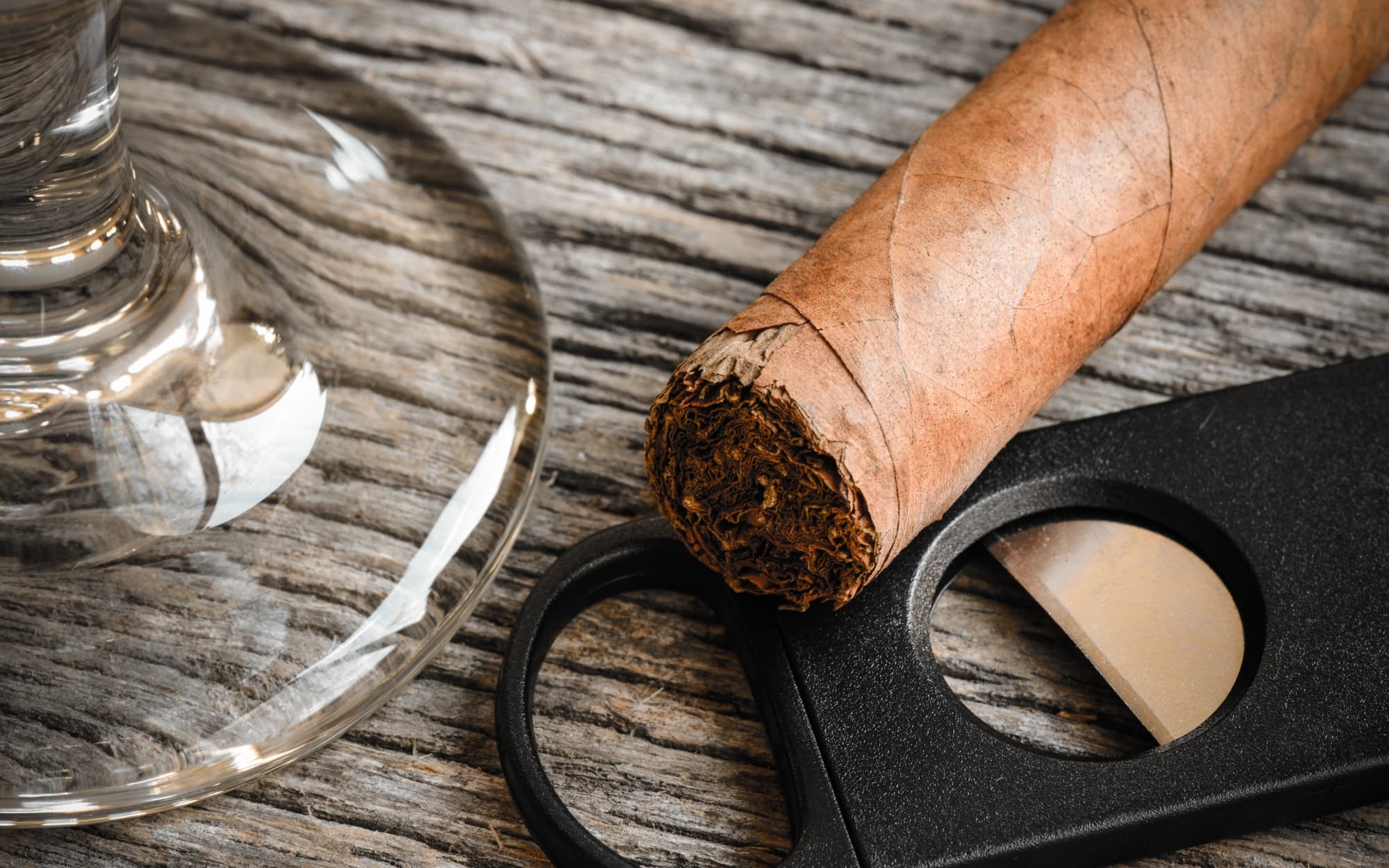Cigar cutter next to an unlit cigar and drinking glass.